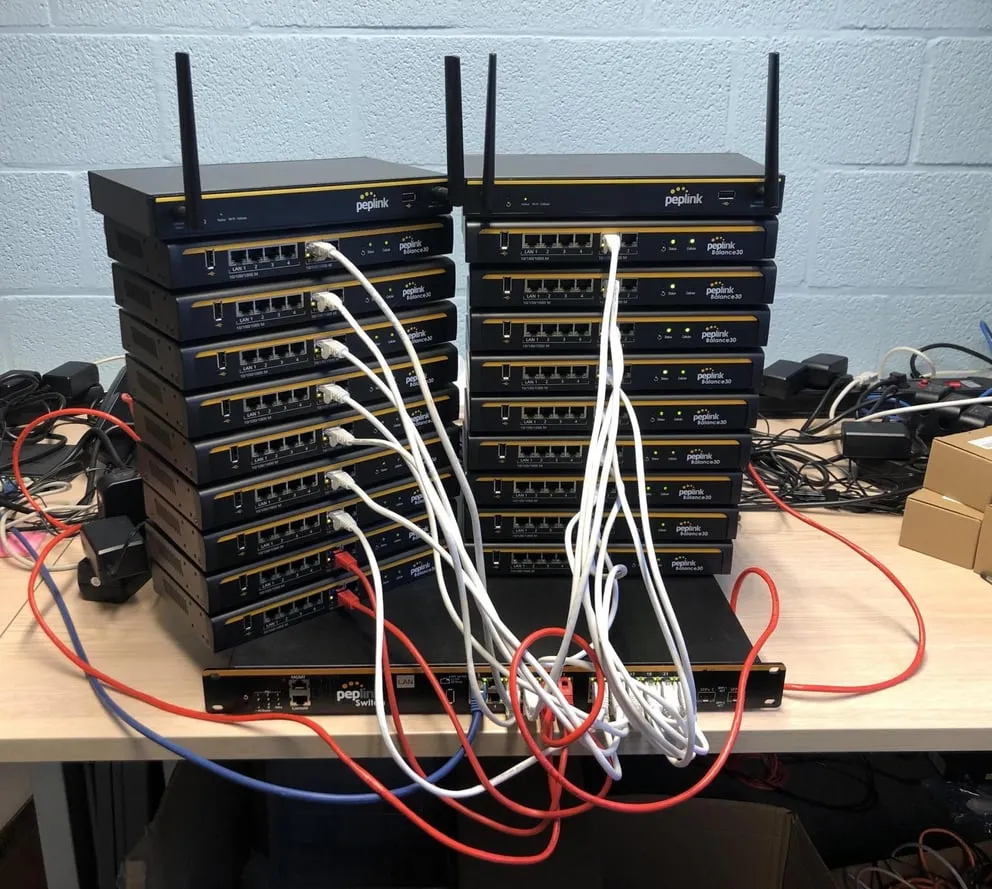 Licenza FIPS per Balance 310, stack di router Peplink Balance 30 con antenne e switch Pepwave su scrivania con cavi