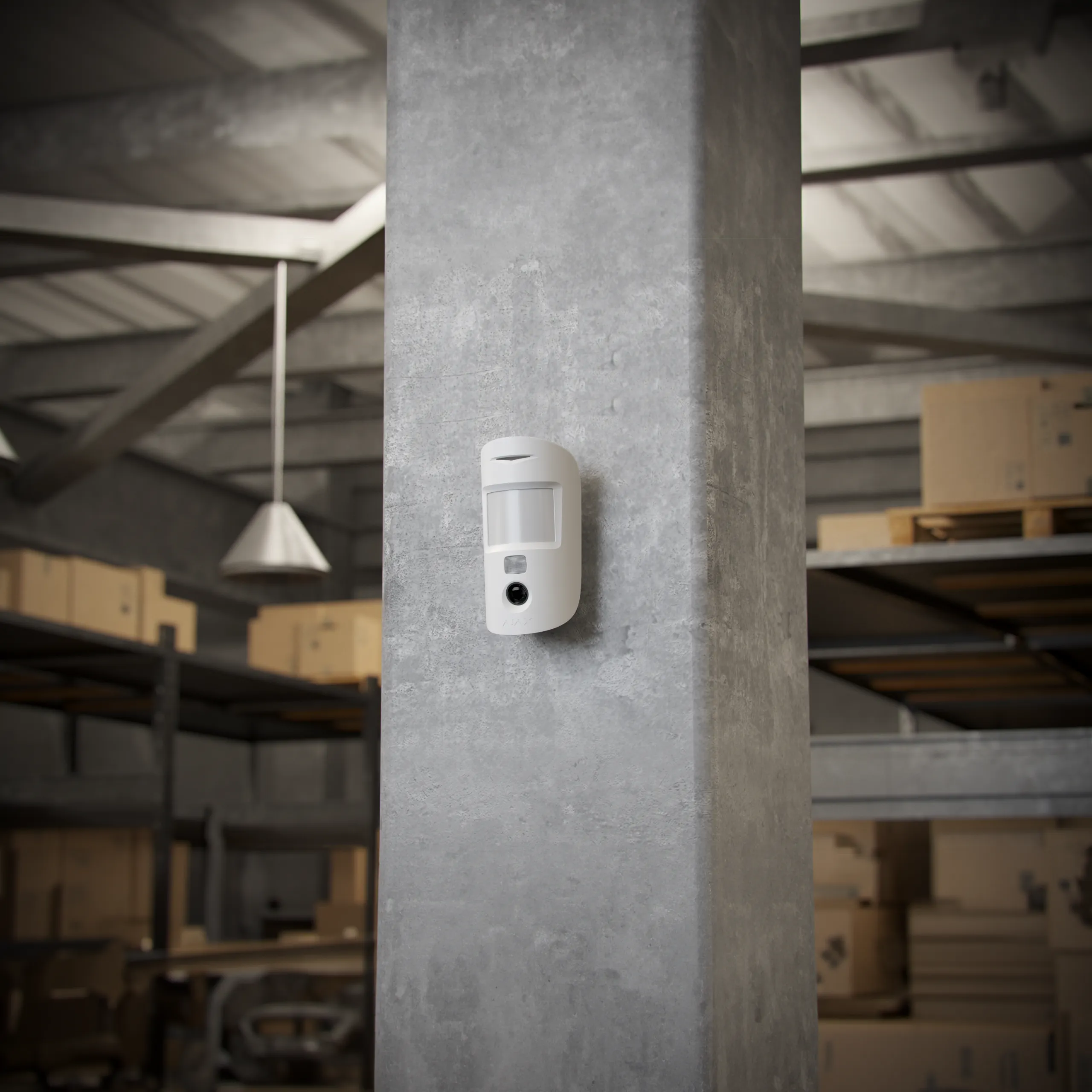 Caméra de sécurité blanche AJAX MotionCam HDR fixée verticalement sur un pilier en béton dans un entrepôt avec capteur de