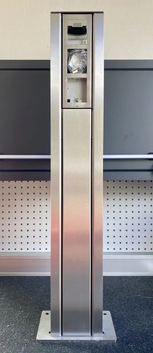Stele in acciaio inox 2N IP Verso con vano elettronico aperto su pavimento grigio per accesso a componenti interni. Stele in acciaio inox 2N IP Verso con vano elettronico aperto su pavimento grigio per accesso a componenti interni.