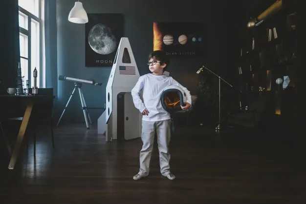 Ragazzo con casco spaziale osserva poster AR Curiscope MINT Mond in stanza con razzo di cartone e telescopio.