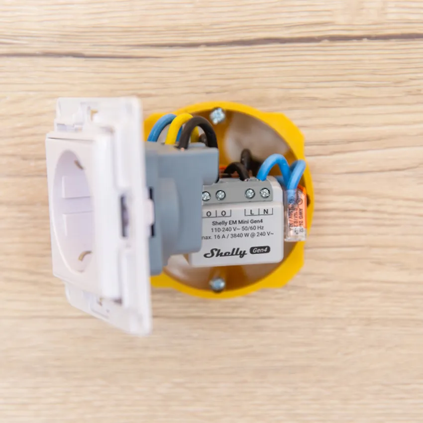 Shelly EM Mini Gen4 smart relay module installed in a yellow wall socket box with connected wires and European power socket