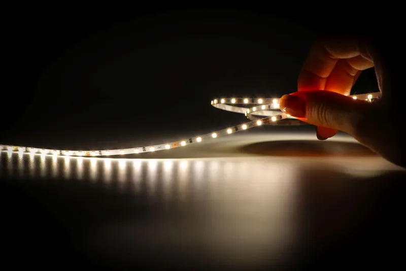Гибкая светодиодная лента Synergy 21 LED Flex Strip 2022 с тёплым белым светом в руке на тёмном фоне создаёт яркие световые