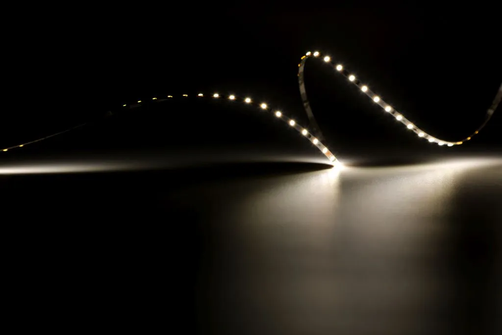 Гибкая светодиодная лента Synergy 21 LED Flex Strip 2022 с тёплым белым светом, изогнутая волной на чёрном фоне для