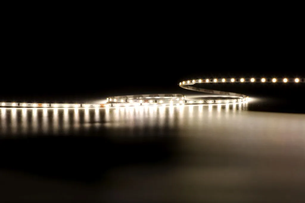 Гибкая светодиодная лента Synergy 21 LED Flex Strip 2022 с тёплым белым светом на тёмной отражающей поверхности под низким