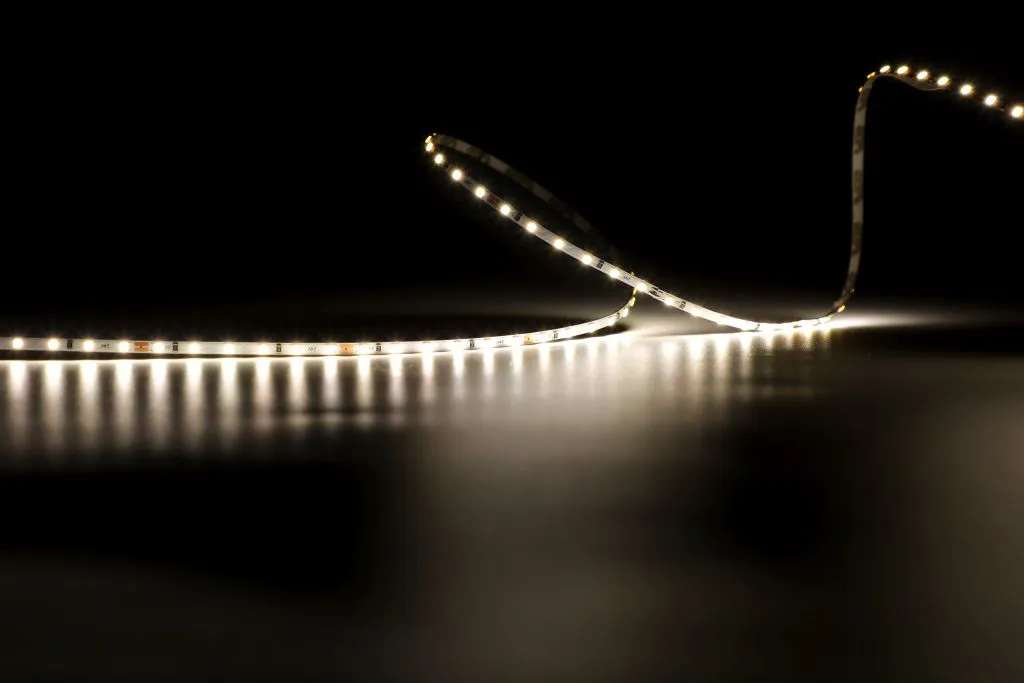 Гибкая светодиодная лента Synergy 21 LED Flex Strip 2022 с тёплым белым светом на чёрном фоне изогнута S-образно с