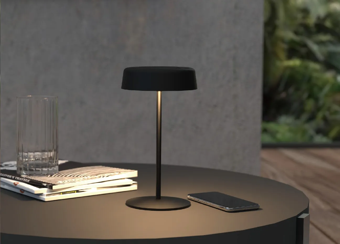 Lámpara de mesa negra Synergy 21 LED SOLAR con base circular, pantalla plana y luz cálida en mesa exterior junto a libros y Lámpara de mesa negra Synergy 21 LED SOLAR con base circular, pantalla plana y luz cálida en mesa exterior junto a libros y
